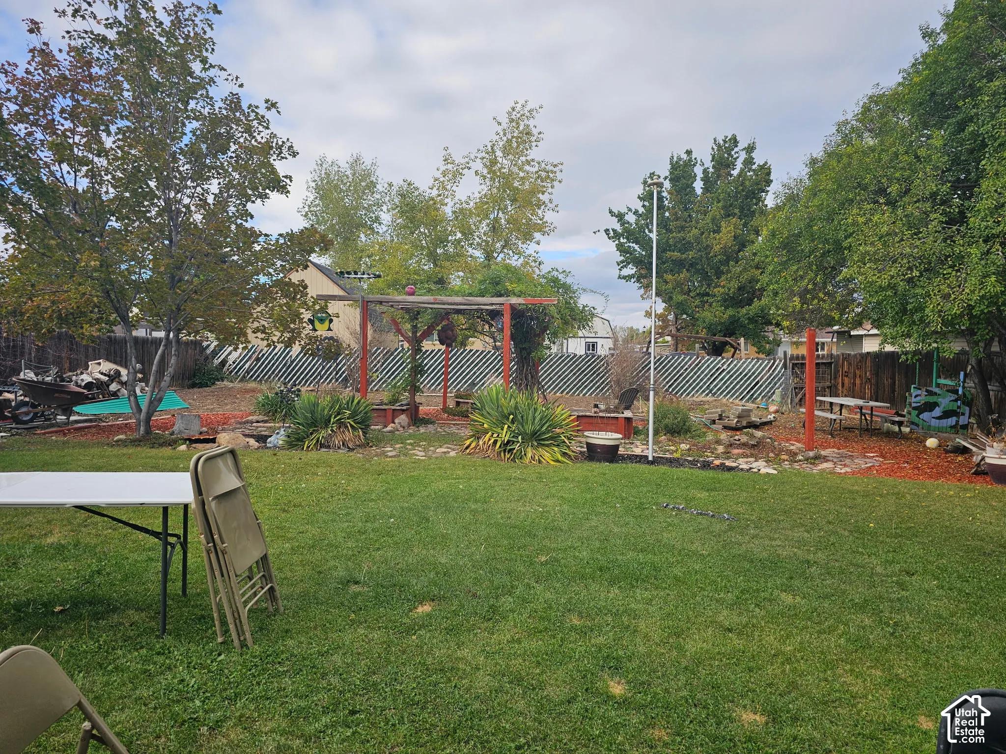 Backyard featuring a grass lawn, decorative red wood chip landscaping, a wooden pergola, and perimeter wood fencing