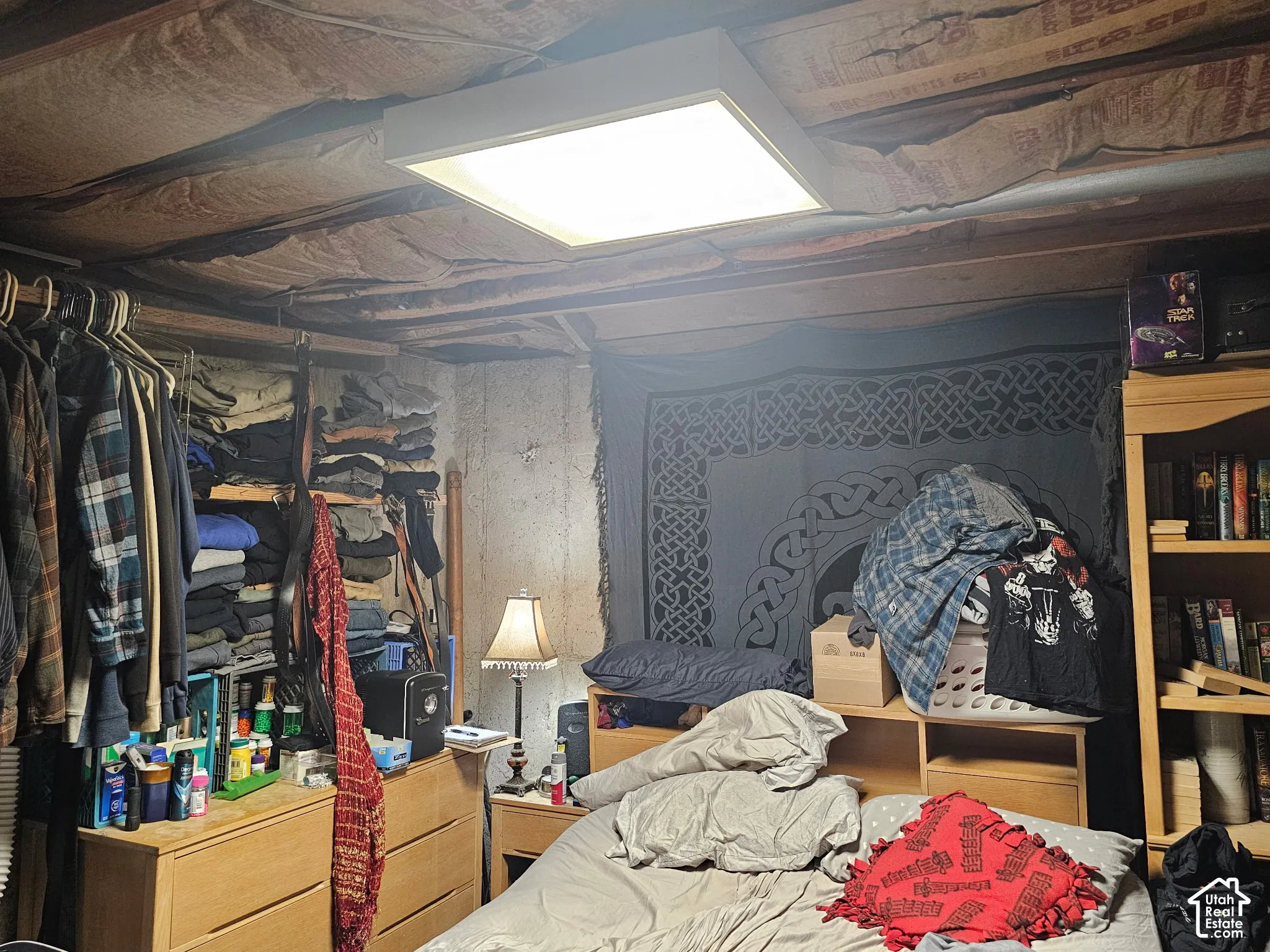 Exposed ceiling joists with insulation, concrete walls, and a recessed square ceiling fixture