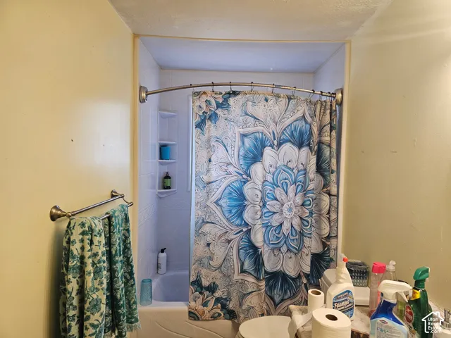 Shower alcove featuring white tile surround, integrated shelving, and a curved shower rod