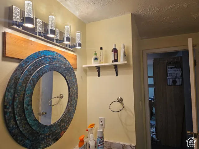 Bathroom vanity area featuring a multi-light fixture with cylindrical glass shades, a decorative circular mirror with mosaic tile detailing, a mounted wall shelf with iron-style brackets, and a circular metal towel ring
