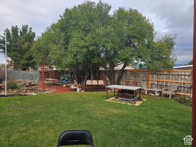 Expansive backyard featuring a manicured lawn, mature trees, wood privacy fencing, and a dedicated stone-paved fire pit area