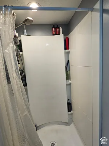 Shower enclosure featuring curved white wall panels, integrated corner shelving, and a handheld shower fixture