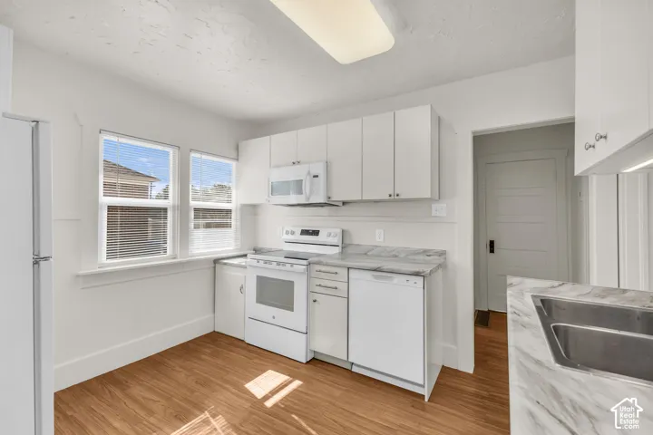 Kitchen featuring white cabinetry, wood-finish flooring, stone-patterned laminate countertops, double-basin stainless steel sink, and white appliances
