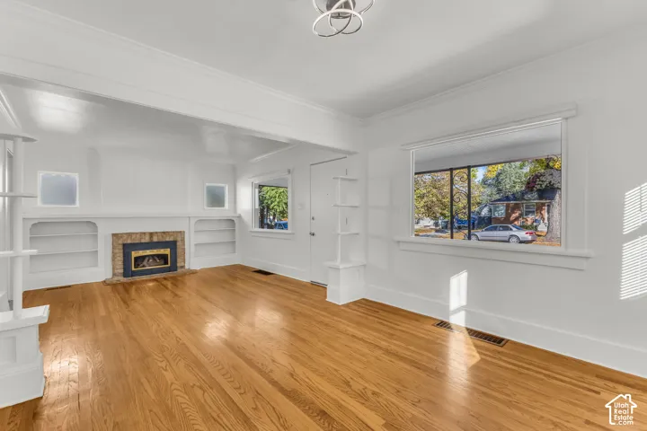 Living area featuring wood-finish flooring, a masonry fireplace with built-in flanking bookshelves, and crown molding