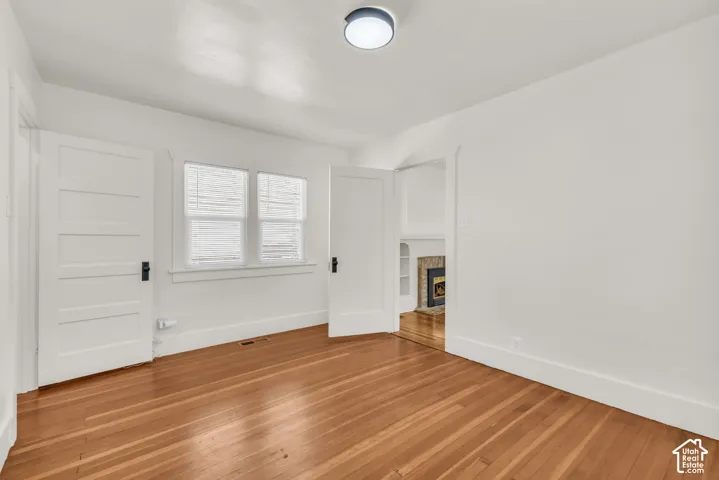 Room featuring wood-finish flooring, two white five-panel interior doors, dual windows with blinds, and a flush-mount light fixture