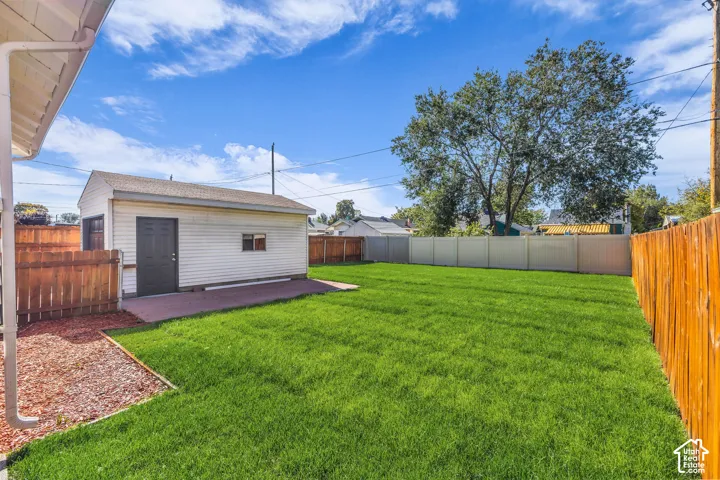 Expansive backyard featuring a manicured lawn, detached garage, wood-style privacy fencing, and a concrete patio area