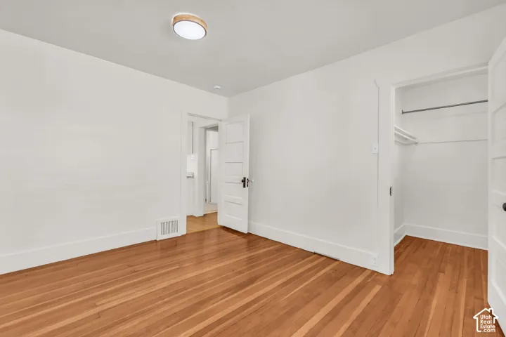Wood-finish flooring, five-panel interior door, ceiling-mounted light fixture, and walk-in closet with built-in shelving