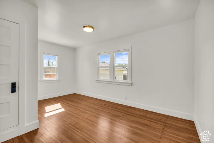 Interior room featuring wood-finish flooring, multi-pane windows with white trim, a five-panel interior door with a matte black lever, and a flush-mount circular ceiling light