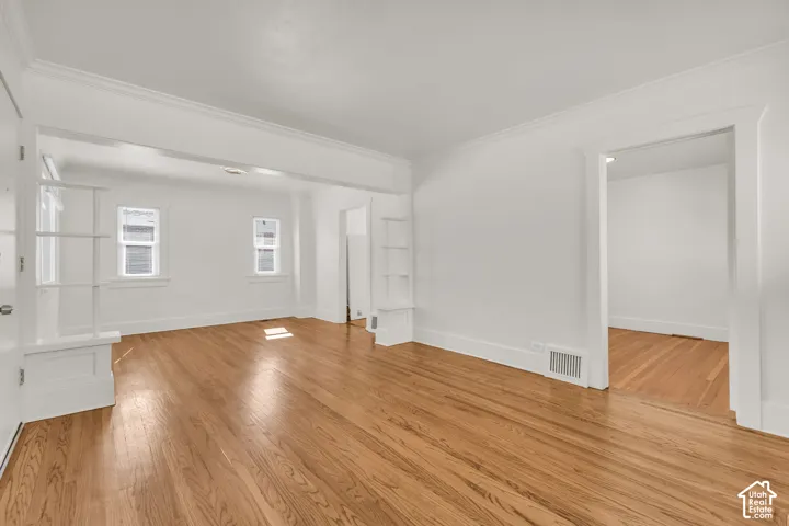 Living area featuring wood-finish flooring, built-in shelving, crown molding, and painted door casings