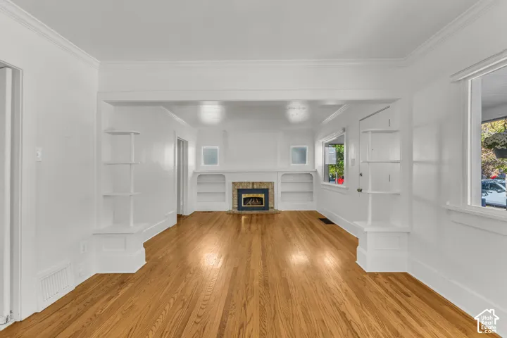 Living space featuring wood-finish flooring, a fireplace with a stone surround, built-in shelving, and crown molding