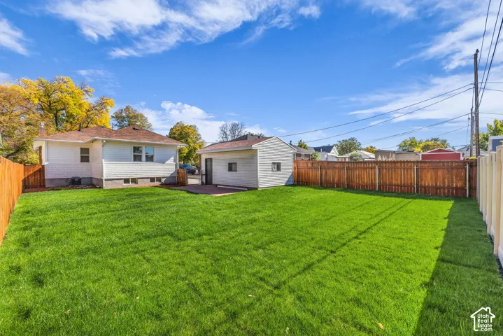 Private backyard featuring a manicured lawn, detached garage, paved patio area, and full-perimeter wood fencing