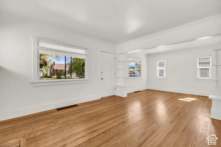 Living area featuring wood-finish flooring, white walls, multiple windows with crisp trim, and built-in shelving