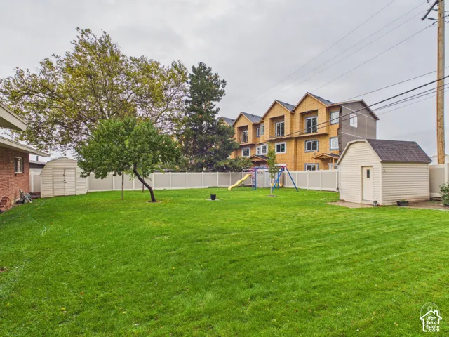 Expansive backyard featuring a lawn, perimeter vinyl fencing, and two detached storage structures