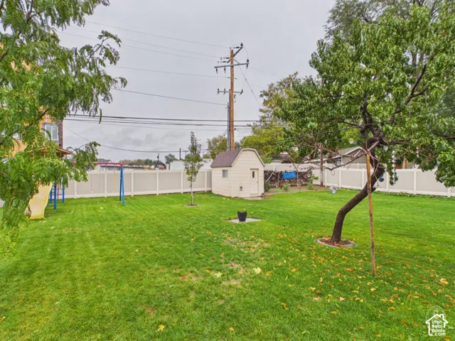 Expansive backyard featuring a level lawn, mature trees, a detached storage shed, and a full-perimeter privacy fence