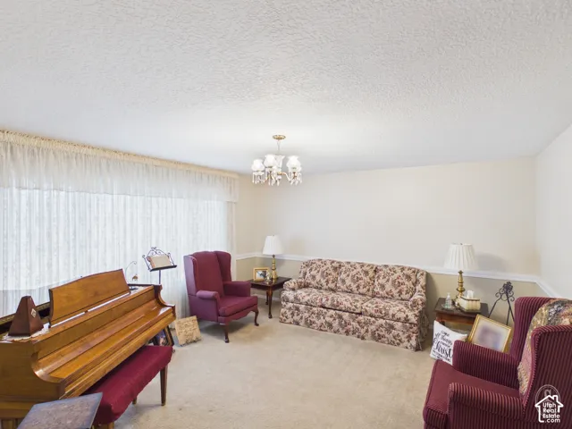 Expansive living area featuring neutral wall-to-wall carpeting, chair rail molding, a large picture window, and a multi-arm chandelier