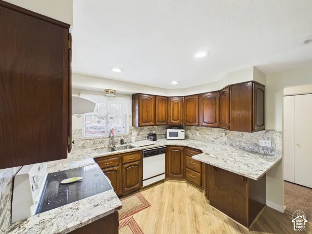 Kitchen featuring stained wood cabinetry, light-toned stone-patterned countertops, wood-finish flooring, recessed lighting, and a stainless steel dual-basin undermount sink
