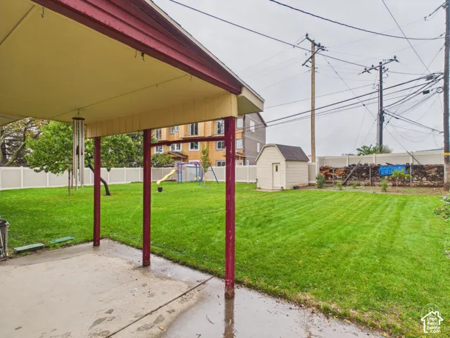 Covered concrete patio featuring a backyard with a vinyl privacy fence, a lawn, and an exterior storage shed