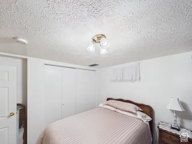 Room featuring textured ceiling, tri-light flush-mount fixture, and double-door closet with white finish