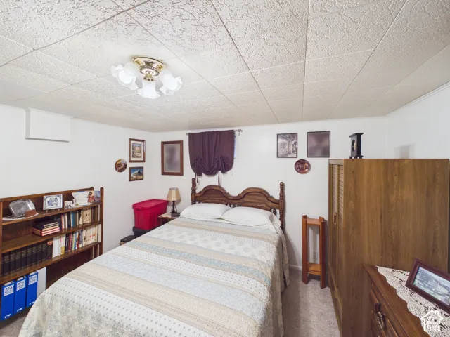 Textured drop ceiling with an attached multi-bulb flush mount light fixture, wall-to-wall carpeting, and panel walls