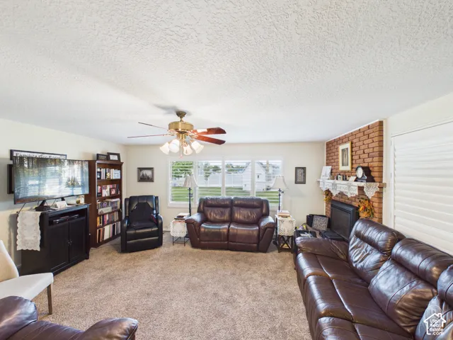 Living area featuring a floor-to-ceiling brick fireplace with a wood mantel, multi-pane windows, and a ceiling fan with integrated lighting