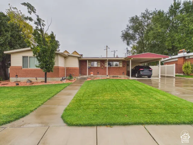 Mid-century ranch exterior featuring red brick and horizontal siding, attached carport, concrete driveway, and manicured front lawn