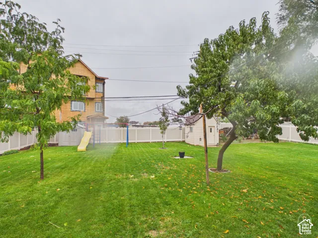 Backyard featuring a manicured lawn, mature trees, a detached storage structure, and a full-perimeter vinyl fence