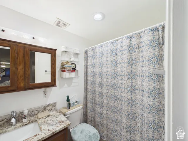 Bathroom featuring a vanity with stone-patterned countertop, wood-finish cabinetry, built-in medicine cabinet, and recessed ceiling lighting