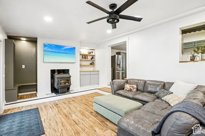 Wood-finish flooring, matte black ceiling fan, wood-burning stove with integrated shelving, and recessed lighting