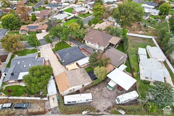 Aerial perspective of a property featuring a concrete driveway, multi-level shingled roofing, mature landscaping, and a metal carport structure