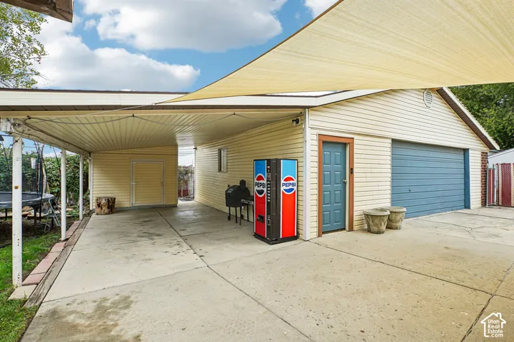 Attached carport with concrete flooring, covered detached garage featuring a blue roll-up door, and a retractable shade sail canopy