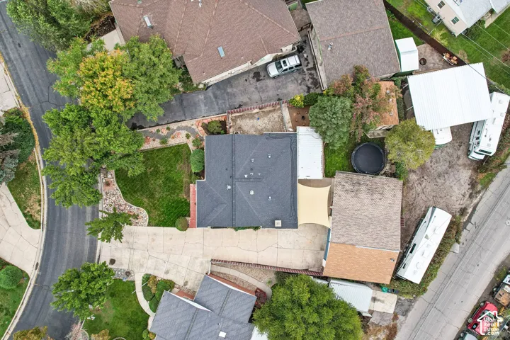 Aerial perspective featuring an asphalt shingle roof, a concrete driveway, a manicured lawn, and mature trees