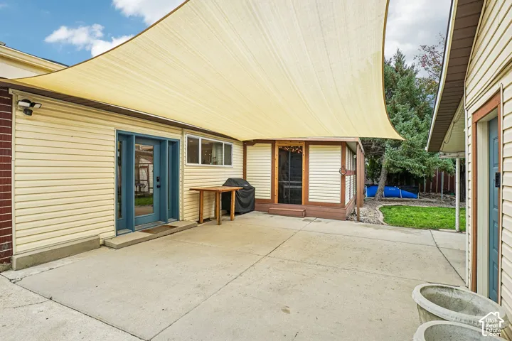 Concrete patio featuring a retractable shade sail, light-colored horizontal siding, and exterior wall-mounted lighting