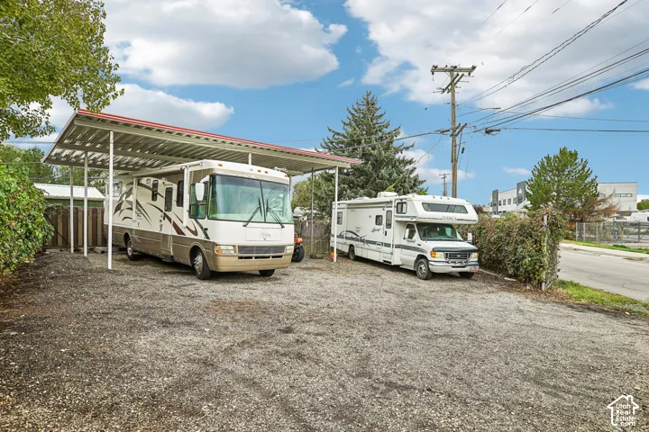 Gravel parking area featuring a metal-framed carport structure and chain-link fencing