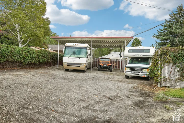 Gravel parking area featuring a metal-roofed carport structure and mature perimeter landscaping