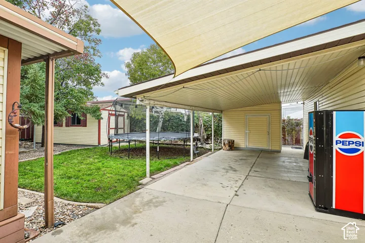Concrete patio with attached overhead cover, tension fabric shade sail, dedicated storage shed, and manicured lawn area
