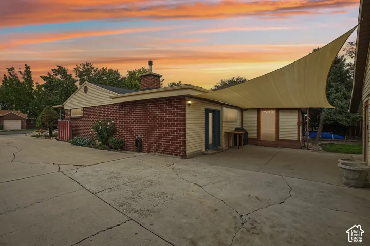 Exterior featuring a multi-material facade of brick and horizontal siding, a masonry chimney, expansive concrete patio, and a tension shade sail