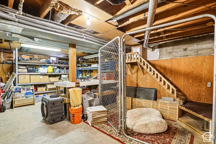 Unfinished basement featuring exposed ceiling joists, wood-panel wall treatments, concrete flooring, and built-in wood stair components