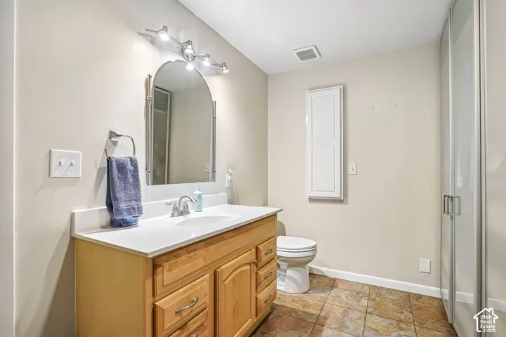 Vanity featuring a light wood-finish cabinet with drawers, integrated solid-surface countertop with an oval basin, arched wall mirror, multi-light fixture, and stone-tile flooring