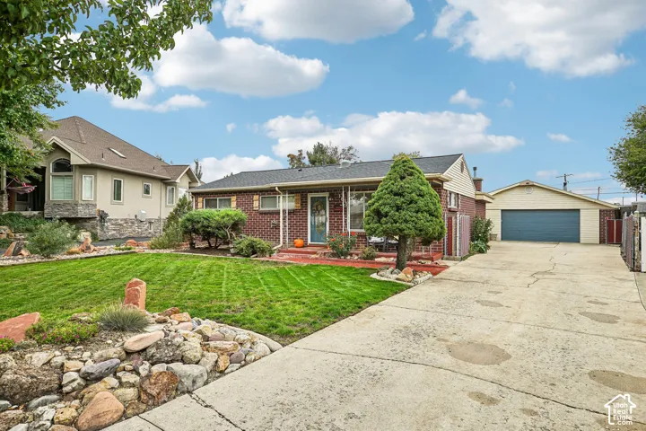 Brick exterior residence featuring a covered front porch, low-maintenance rock landscaping, a manicured lawn, and a detached two-car garage