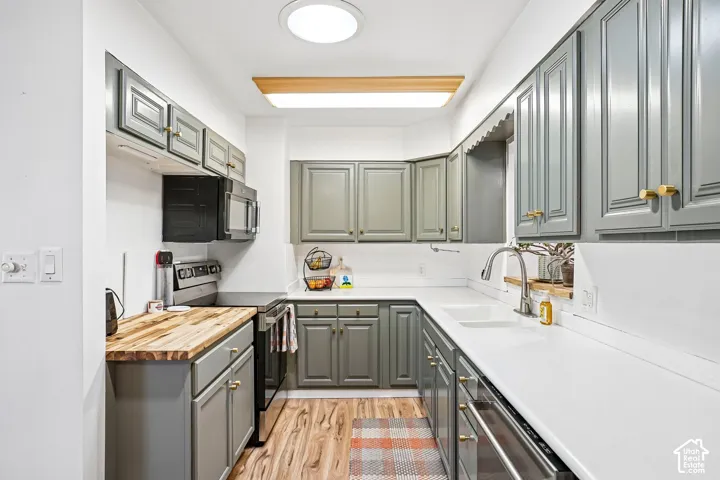 Kitchen featuring grey shaker-style cabinetry, solid-surface countertops, a butcher block section, double-basin sink with a gooseneck faucet, and wood-finish flooring