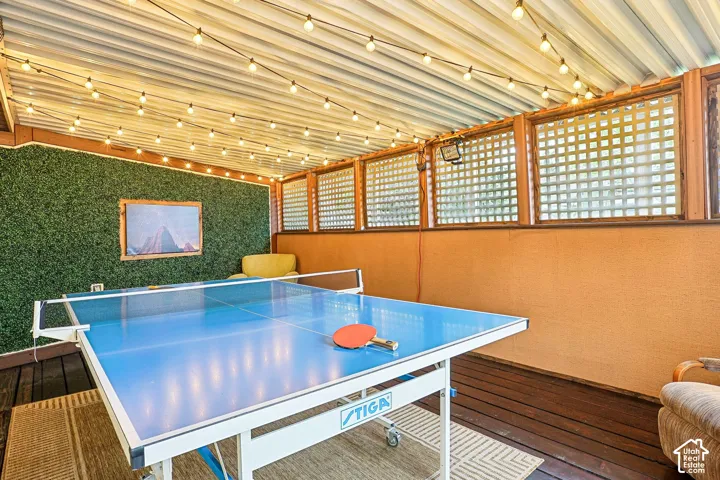 Covered patio featuring wood-finish flooring, string lighting, lattice screening, and an artificial grass feature wall