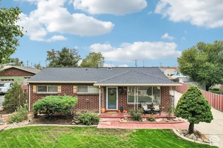 Brick exterior residence featuring a covered front porch, asphalt shingle roof, large picture window, and landscaped front yard with stone-edged garden beds