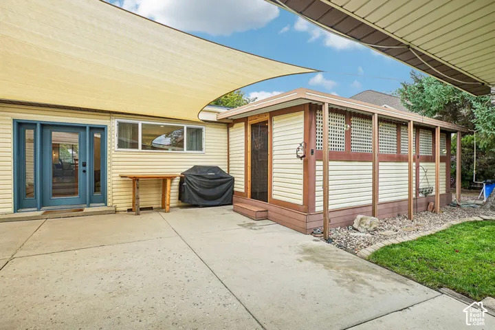 Concrete patio featuring a retractable shade sail, exterior siding, and an attached screened enclosure with lattice detailing