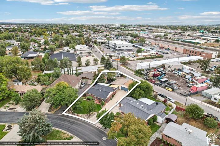 Aerial perspective featuring a single-story residence, asphalt shingle roof, expansive front lawn, paved driveway, and mature trees
