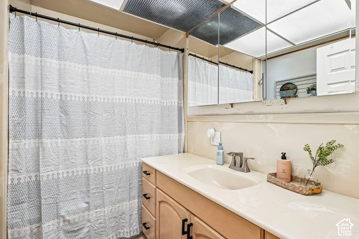 Bathroom vanity featuring a solid-surface countertop with an integrated basin, wood cabinetry, large wall-spanning mirror, and a recessed ceiling lighting panel