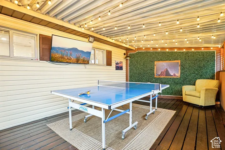 Covered outdoor patio featuring a corrugated metal ceiling, string lighting, dark-stained wood decking, and a decorative faux-foliage accent wall