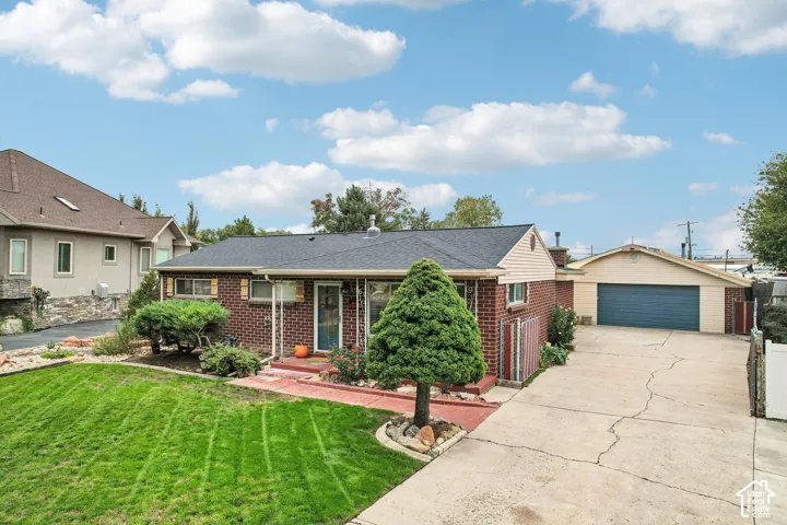 Single-story brick exterior featuring a shingled roof, front lawn landscaping, a paved driveway, and a detached garage