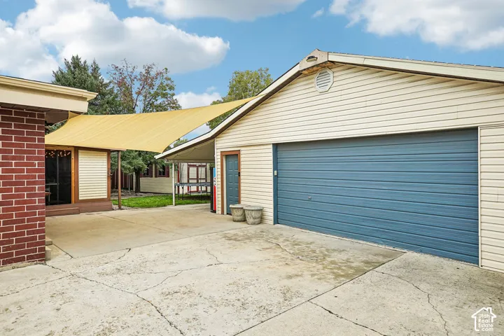 Exterior featuring a brick and vinyl siding facade, a detached garage with a blue overhead door, a concrete driveway, and an attached covered patio area