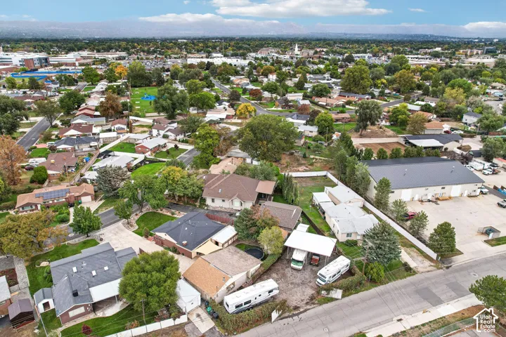 Aerial perspective of a residential property featuring an expansive gravel parking area, a detached covered parking structure, a manicured lawn, and mature trees