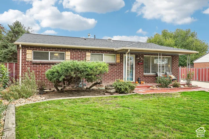 Brick exterior featuring a covered front porch, low-slope shingled roof, decorative window shutters, and a front yard with manicured landscaping